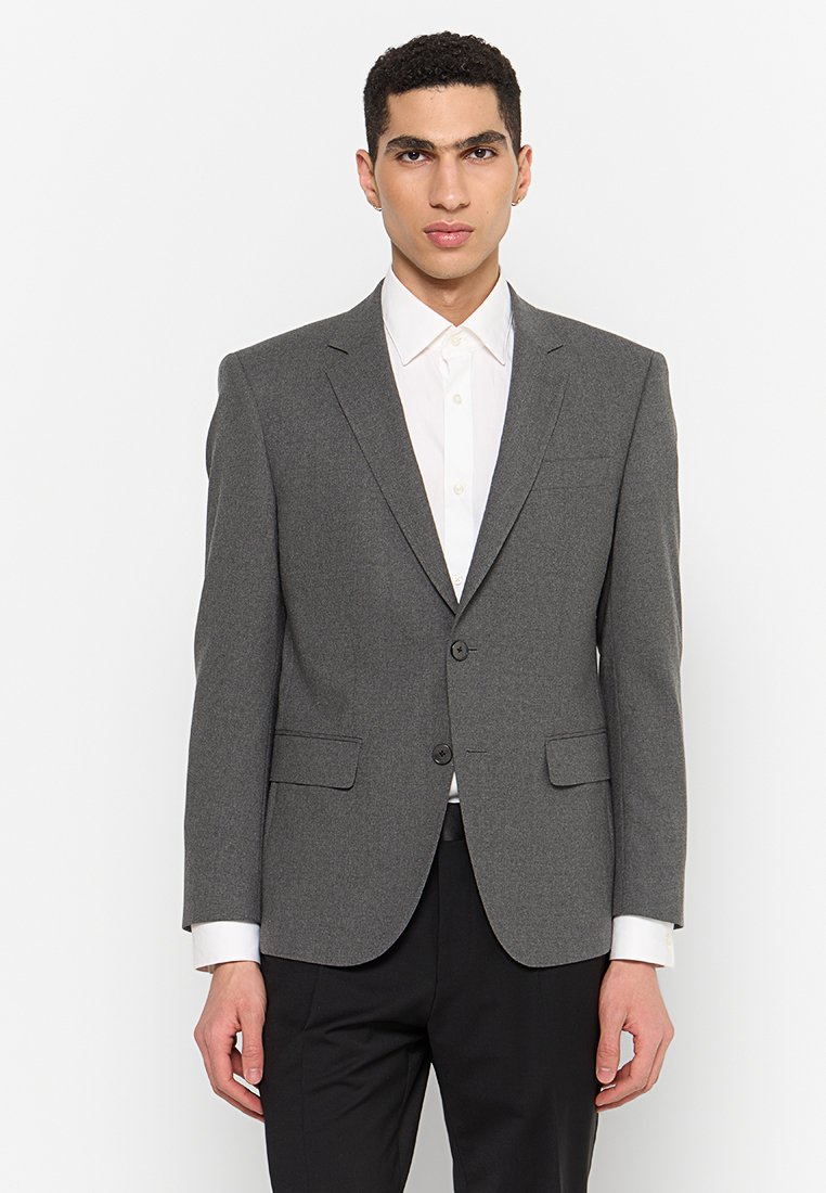 Blazer gris ajusté avec revers en notch, fermeture à un bouton, deux poches avant et texture lisse, porté sur une chemise blanche.