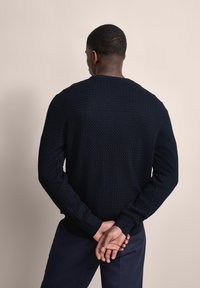 Maritimer, gestrickter Pullover mit strukturiertem Muster und langen Ärmeln, mit Rundhals und gerippten Bündchen. Modell von hinten gesehen.