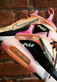 Sneakers med en gradient av orange och rosa på ovandelen, svarta sidor, rosa transparent sula, synlig luftdämpning och kontrasterande sömnadsdetaljer.