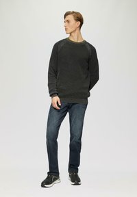 Dunkelgrauer Strickpullover mit geripptem Struktur, grüner Rundhalsausschnitt, kombiniert mit dunkelblauen Jeans und schwarzen Sportschuhen. Lockere Passform.