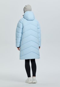 Abrigo acolchado azul claro con diseño en chevron, capucha y mangas largas. Combinado con leggins negros y zapatillas blancas. Textura suave.