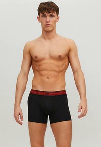 Svarte boxershorts med en rød merkebånd i midjen, tettsittende design, laget av glatt stoff, som gir et minimalistisk utseende.
