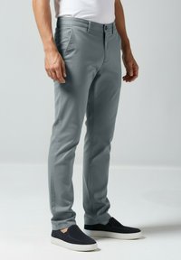 Lichtgrijze slim-fit broek gemaakt van een gladde stof, met een platte voorkant, zijzakken en een knoopsluiting, gecombineerd met donkere instapschoenen.