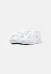 Sneakers in pelle bianca con design a vita bassa. Caratteristiche includono chiusura con lacci, una suola testurizzata e un piccolo logo accentato sul lato.