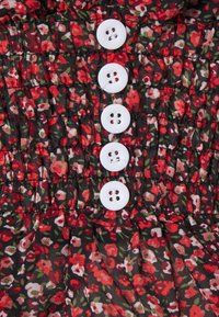 Tissu noir froncé avec un motif floral rouge et blanc ; comporte cinq boutons blancs au centre.