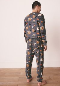 Ensemble de pyjama gris avec motifs d'animaux, comprenant des ours et des chats, agrémenté d'accents saisonniers comme des citrouilles. Matière douce et coupe décontractée.