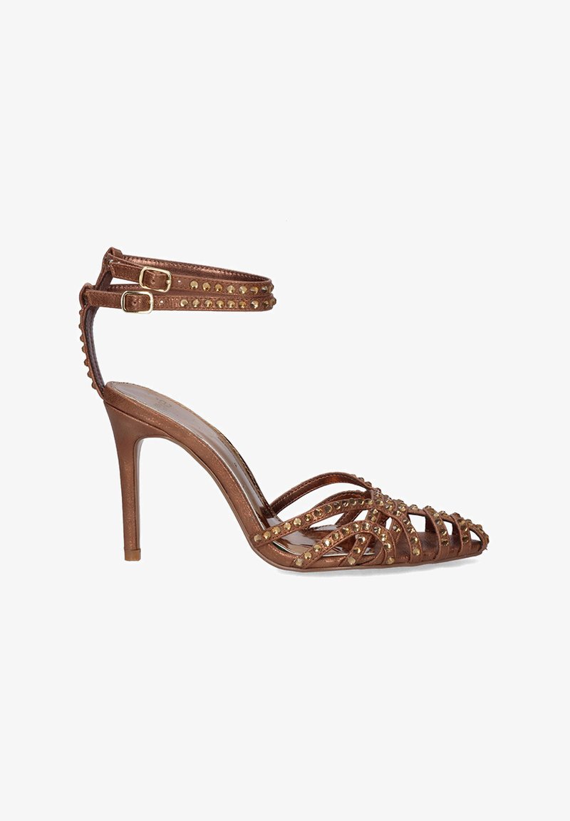 Sándala metálica marrón de tacón alto con diseño de tiras en forma de cruz, correas en los tobillos y acentos de tachuelas doradas. Punta afilada y silueta elegante.