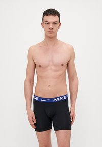 Fekete boxer alsónadrág kék Nike márkájú derékszíjjal. Szoros illeszkedés és sima textúra jellemzi. Egyszerű dizájn, további minták nélkül.