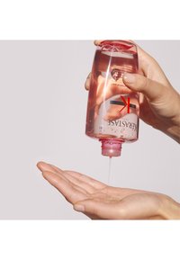 Duidelijke plastic fles met een rode dop, gevuld met roze gel. Hand gepositioneerd om de vloeistof op te vangen terwijl deze uit de fles stroomt.