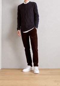 Marinblå kabelstickad tröja, vit skjorta med krage, bruna kordfläskbyxor och vita sneakers. Enkel, strukturerad design med ribbad detalj.