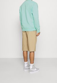 Felpa verde menta, pantaloni corti beige al ginocchio e sneakers alte grigie. Le sneakers presentano dettagli bianchi e un logo, con calze visibili.