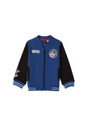 Veste bomber bleue avec des manches noires, des poignets côtelés et des zips. Présente des patchs avec le mot "ROCK" et un logo avec un drapeau britannique.