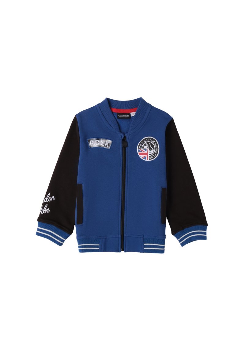 Chaqueta bomber azul con mangas negras, puños acanalados y cremalleras. Presenta parches que dicen "ROCK" y un logo con la bandera británica.
