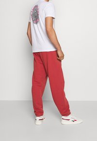 Vit kortärmad t-shirt med en djärv svart och rosa grafik av ett fingeravtryck på baksidan, kombinerad med röda svettbyxor och vita sneakers.