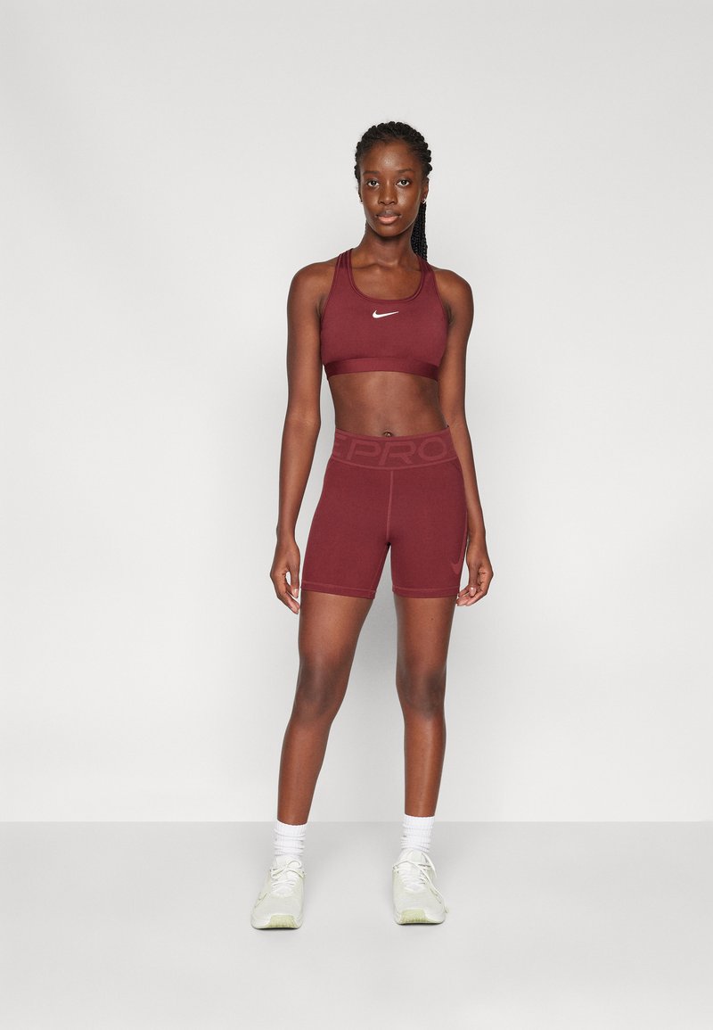 Sport bra bordeaux e pantaloni corti abbinati realizzati in tessuto elasticizzato. Presenta il logo Nike sul bra, con una vita elastica sui pantaloni.