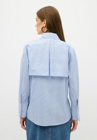 Camicia a maniche lunghe blu e bianca a righe con un design unico sul retro strato, polsini con bottone e tessuto morbido.