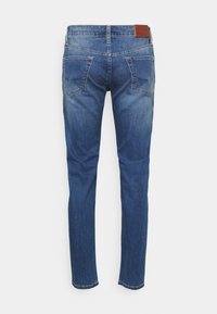 Jeans de denim azul ajustados con un acabado desgastado, cinco bolsillos y un parche de cuero sintético marrón en la cintura trasera. Detalle de costura clásica.