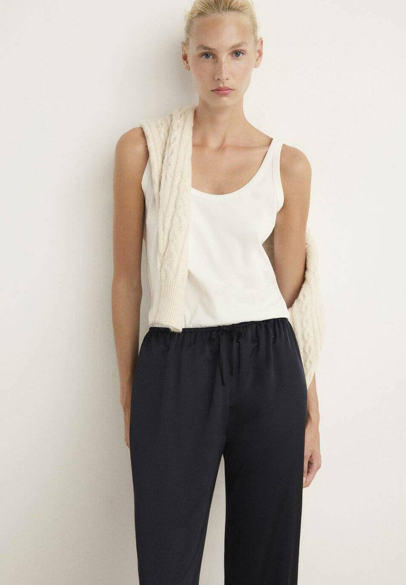 Top blanco sin mangas combinado con pantalones de cintura elástica en color navy, complementado con un cárdigan de punto crema que se lleva sobre los hombros.