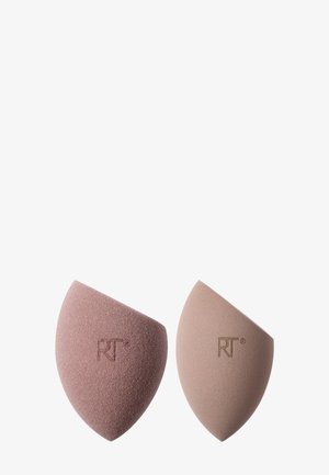 Kaksi kulmavaahto meikkisientä vierekkäin, toinen pölyinen roosa ja toinen vaalea beige, molemmissa kohokuvioitu "RT"-logo.