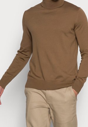 Brauner Rollkragenpullover aus glattem Strickstoff, mit langen Ärmeln und gerippten Bündchen, kombiniert mit hellbeigen Hosen.