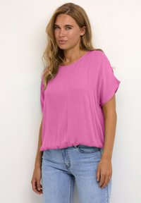 Lyserød kortærmet blouse lavet af letvægtigt stof, med en afslappet pasform og buet kant. Sat sammen med lyseblå denim jeans.