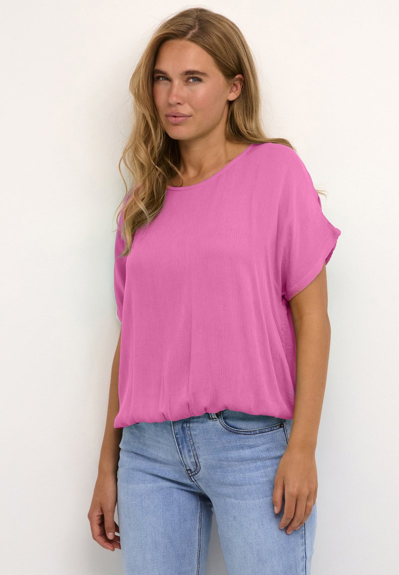 Lyserød kortærmet blouse lavet af letvægtigt stof, med en afslappet pasform og buet kant. Sat sammen med lyseblå denim jeans.