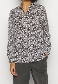 Chemise à manches longues avec boutons, en tissu léger, présentant un motif en losanges bleu marine et crème, avec un col doux et une coupe décontractée.