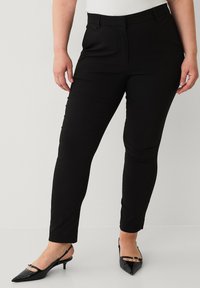 Sorte tapered bukser med en glat overflade, med flad front, sidelommer og en mid-rise talje, parret med glansfulde sorte hæle.