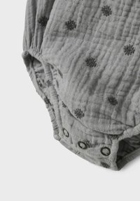 Grå tygromper med en texturerad, skrynklig yta. Har svarta prickiga mönster och metallknappar i botten för enkel påklädning.