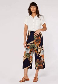 White short-sleeve button-up shirt with chest pocket, paired with navy culottes featuring colorful floral pattern. Brown strappy sandals.