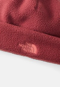 Gorro de fleece vermelho com uma superfície texturizada. Apresenta um logótipo bordado em rosa claro. Forma circular e ajuste justo.