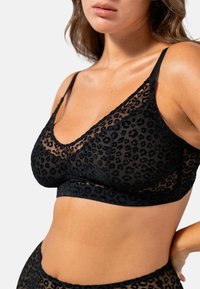 Bralette nera in pizzo con motivo leopardato trasparente, design a V, spalline regolabili e dettagli in texture morbida lungo i bordi.