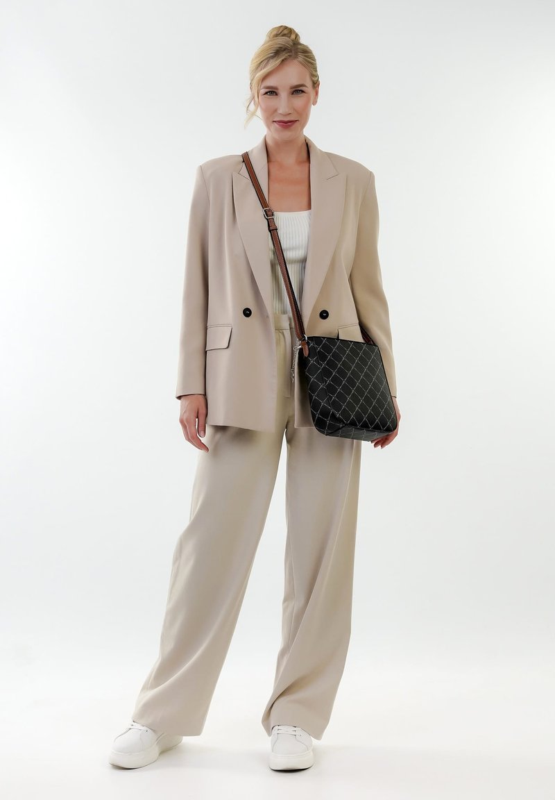 Beiger Blazer mit zwei schwarzen Knöpfen, cremefarbenem Rippoberteil, hellbeigen Hosen und einer schwarzen gesteppte Umhängetasche mit braunem Tragegurt. Weiße Sneakers.