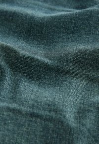 Tissu en denim bleu canard, montrant une texture lisse avec des variations de couleur subtiles et un motif de sergé visible.