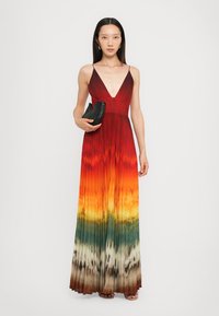 Robe maxi avec un décolleté en V profond, un design plissé et un dégradé de couleurs allant du rouge à l'orange, puis au vert et au marron. Accompagnée d'une pochette noire.