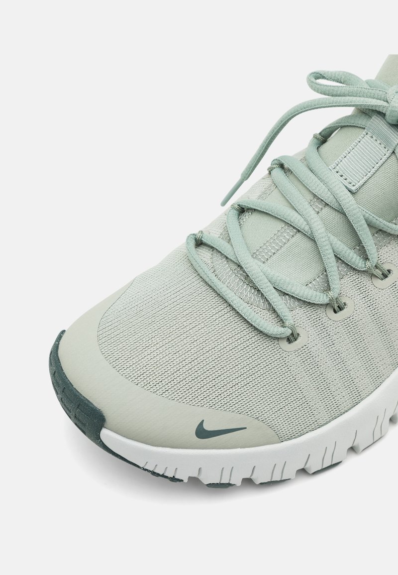 Zapatilla deportiva de color verde claro con parte superior de tela texturizada, diseño con cordones y acentos en verde oscuro contrastantes en la suela y el logo.