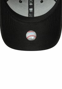 Schwarze Baseballkappe mit gebogenem Schirm, auf der Vorderseite mit einem runden MLB-Aufkleber eines Baseballs versehen. Texturiertes Gewebe und sichtbare Innenauskleidung.