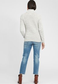 Lichtgrijze gebreide turtleneck trui met een textuurafwerking, gecombineerd met lichtblauwe spijkerbroek en bruine enkellaarsjes.
