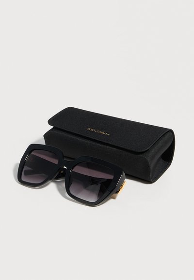 Μαύρα τετράγωνα γυαλιά ηλίου σε μεγάλο μέγεθος με σκούρους φακούς δίπλα σε μαύρη υφασμάτινη σκληρή θήκη Dolce & Gabbana με χρυσό λογότυπο.