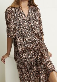 Schwarzes Blumenkleid mit kurzen Ärmeln, das ein lebhaftes Muster aus pinken und weißen Blumen aufweist, knielang und mit bequemer Passform. Glatte Stoffstruktur.