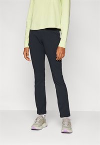 Zwarte outdoorbroek in een slim fit, gemaakt van duurzaam materiaal. Gecombineerd met een lichtgroene lange mouw top en beige sneakers met paarse accenten.