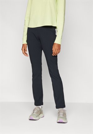 Pantalons noirs de plein air à coupe ajustée, fabriqués dans un matériau durable. Associés à un haut à manches longues de couleur vert clair et à des baskets beiges avec des accents violets.