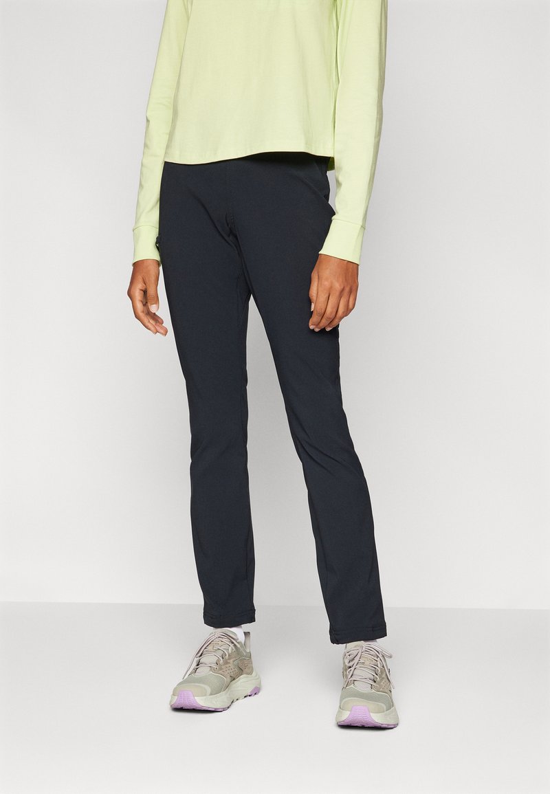 Zwarte outdoorbroek in een slim fit, gemaakt van duurzaam materiaal. Gecombineerd met een lichtgroene lange mouw top en beige sneakers met paarse accenten.