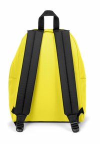 Gul ryggsäck med svarta vadderade remmar, ett handtag upptill och slät yta. Har sidofickor och justerbara remmar för komfort.