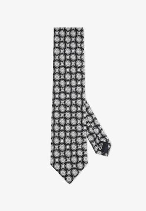 Czarny krawat z powtarzającym się białym wzorem florystycznym i geometrycznym. Wykonany z gładkiego materiału z zakończeniem w szpic i metką na wąskim końcu.
