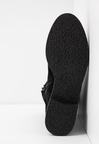 Botte de cheville en daim noir avec une semelle en caoutchouc texturée. Fermeture à glissière latérale. L'intérieur est doté d'une doublure lisse. Design simple et discret.