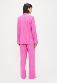 Ροζ ριγέ πιτζά�μες με κομπίνες κουμπιών, μακριά μανίκια και φαρδιά παντελόνια, και τα δύο με λευκές λεπτομέρειες.