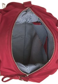 Punainen kangaskassi, jossa on vetoketjulla avattava osio, ja jossa on raidallinen sinivalkoinen vuori sekä pieni tasku.