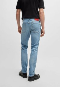 Ljusblå jeans i denim med rak benmodell, med en röd logopatch på midjebandet och standard bakfickor.