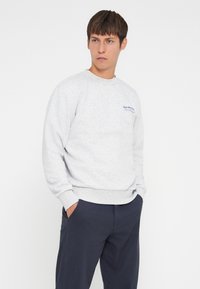 Gray sweatshirt with a crew neck, long sleeves, and ribbed cuffs. Features a subtle blue logo on the left chest. Soft, textured fabric.